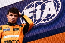 norris holding his head in front of an FIA sign