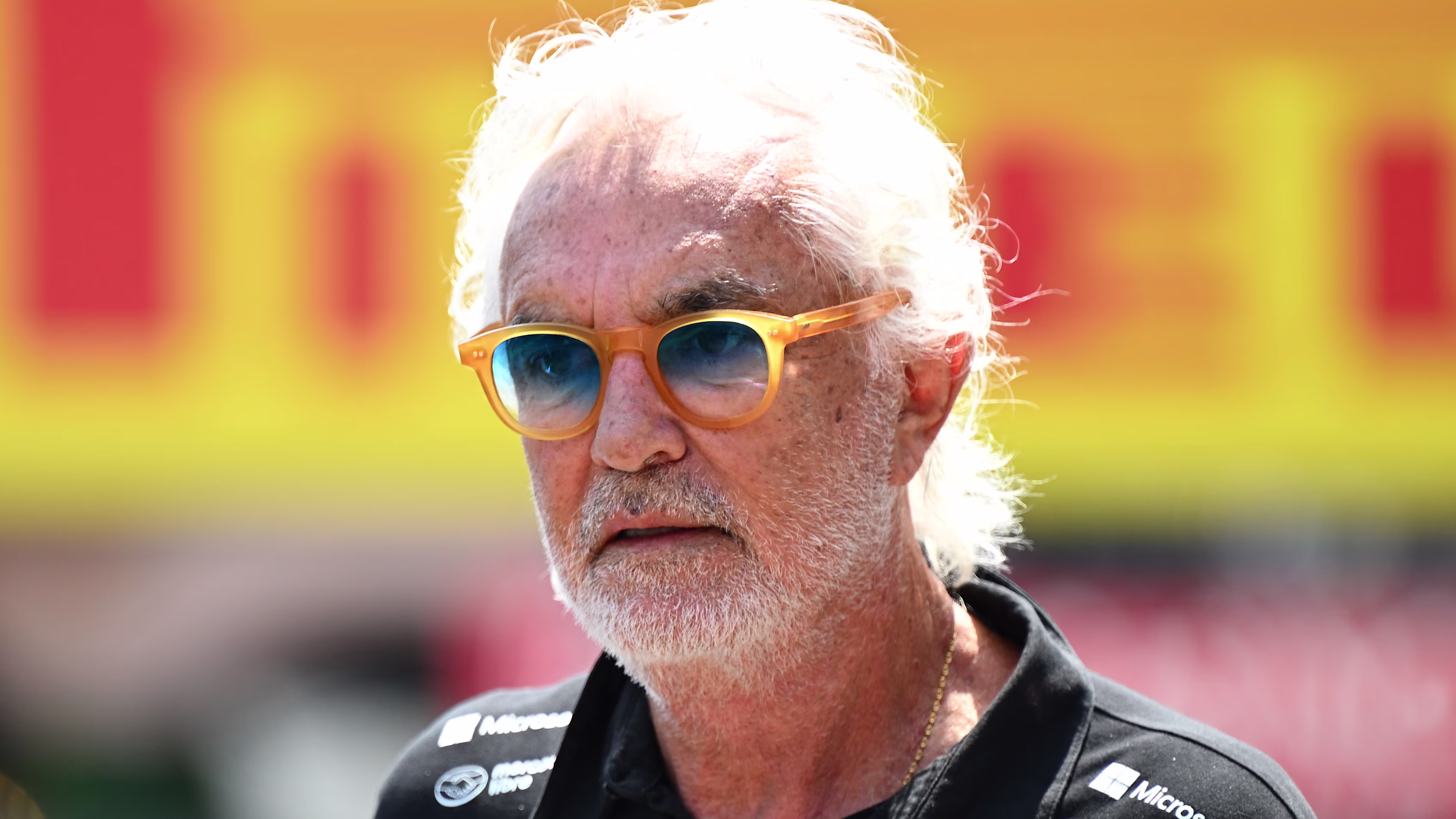 Flavio Briatore wearing his sunglasses and Alpine F1 team wear in front of a Pirelli sign