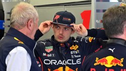 Verstappen holds his cap whilst looking at Helmut Marko